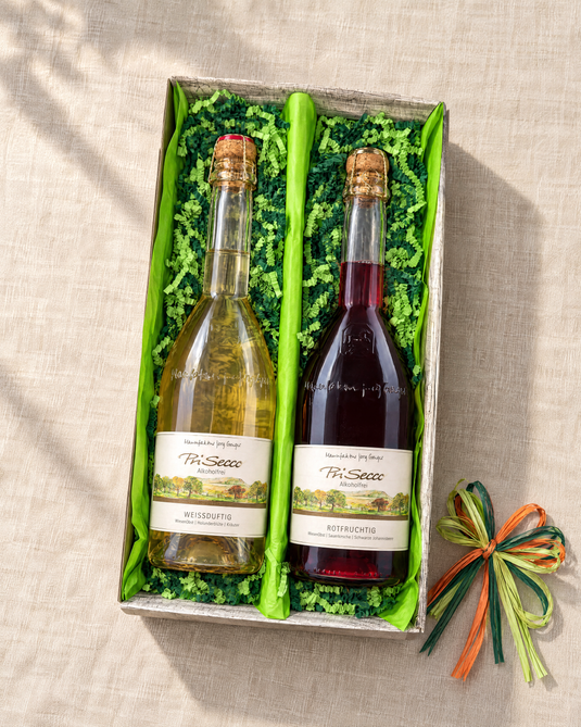 PriSecco Geschenkset mit Weißduftig und Rotfruchtig im offenen Zweierkarton, hellgrünem Papier, grüner Papierwolle und dreifarbiger Bastschleife