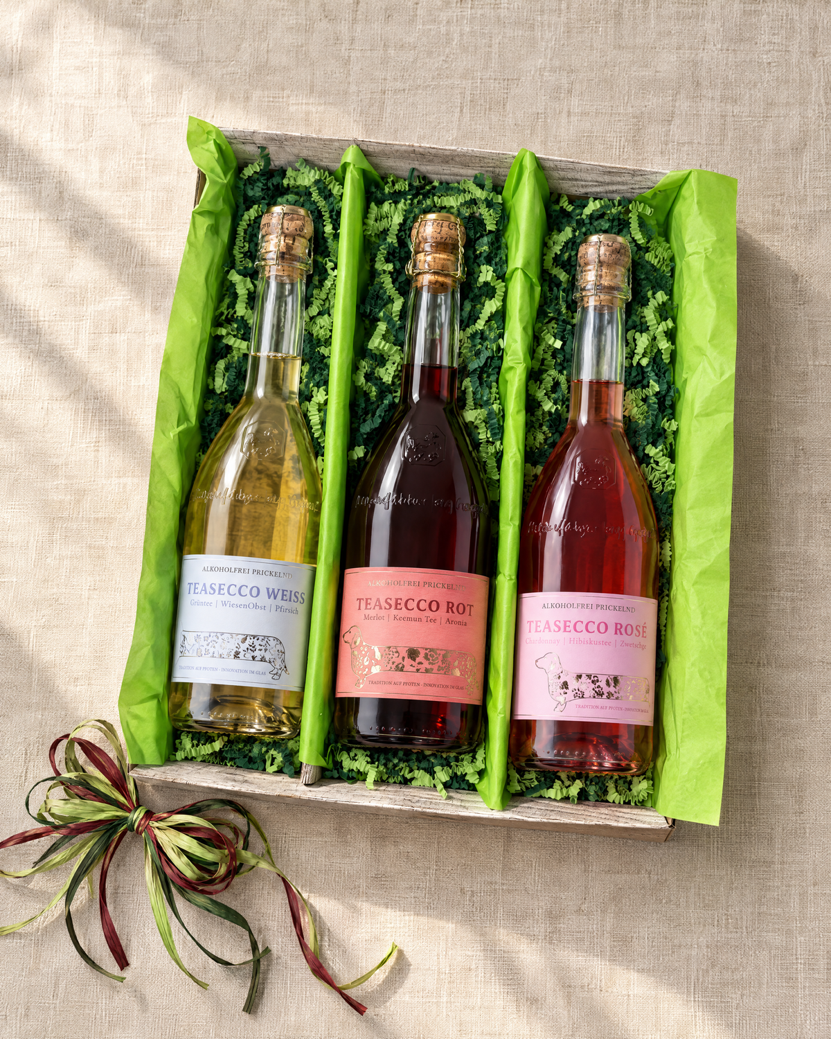 TeaSecco Trio Geschenkset mit Weiß, Rot und Rosé in einer 3er-Kartonage mit grünem Papier und dreifarbiger Bastschleife